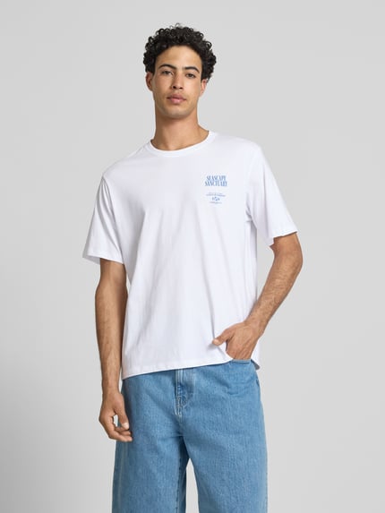 Męskimodel nosi relaxed fit męski t-shirt z bawełny, model 'Photo' z nadrukiem z napisem Jack & Jones, okrągły dekolt, długość tyłu 70 cm, widok całej sylwetki z przodu.
