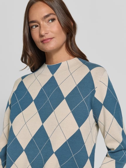 Modelka prezentuje sweter z dzianiny 'Strickpullover aus Viskose-Mix im Allover-Look' od COMMA, mieszanka wiskozy, krój regular fit, wzór na całej powierzchni, stójka, długość tyłu w rozmiarze 36: 53 cm, długość rękawów w rozmiarze 36: 58 cm, odcienie beżu i niebieskiego, geometryczne romby, gładka tekstura, zbliżenie górnej części ciała.