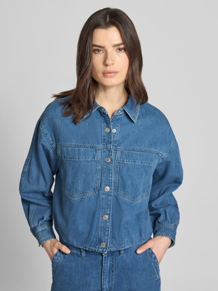 Frauenmodel trägt Jeansjacke mit Brusttaschen Modell 'Imke' von JOOP!, Reine Baumwolle, Relaxed-Fit, Hemdblusenkragen, Knopfleiste, mittleres Blau, strukturierte Oberfläche, Ganzkörperansicht von vorne.