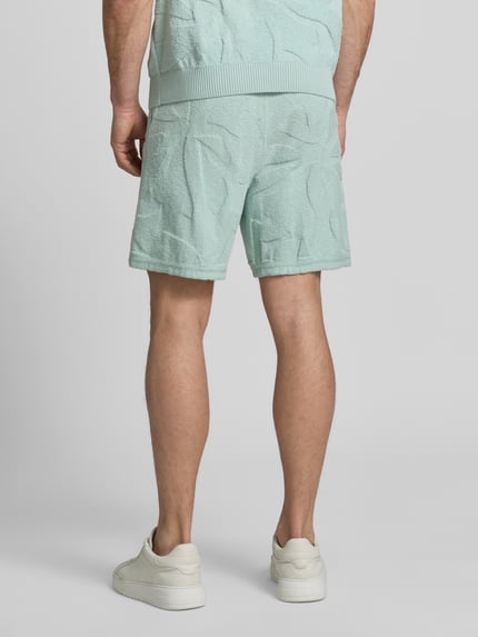 Männermodel trägt Regular Fit Sweatshorts aus Baumwoll-Mix Modell 'ASURFER' von BOSS Orange in Optik: Unifarben mit Struktur, Label-Patch, elastischem Bundabschluss mit Tunnelzug, Eingrifftaschen, Materialverarbeitung: Frottee, Farbe Hellblau, Ganzkörperansicht Rückansicht.