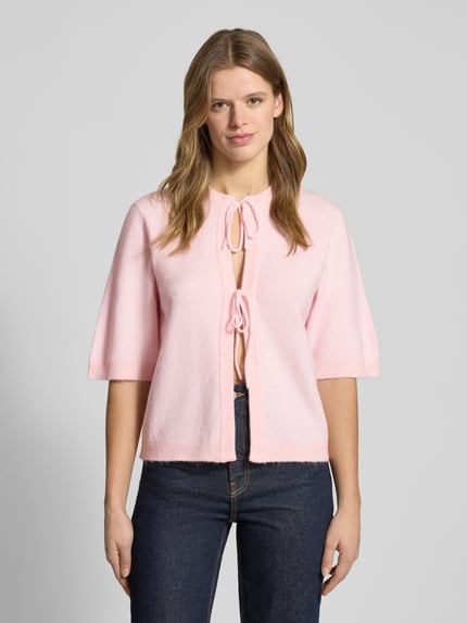 Vrouwenmodel draagt Regular Fit Cardigan met schnürungen model 'SIMONI' van Only in effen roze breistructuur, ribboorden, half lange mouwen, ronde hals, label stitching detail. Vooraanzicht bovenlichaam.