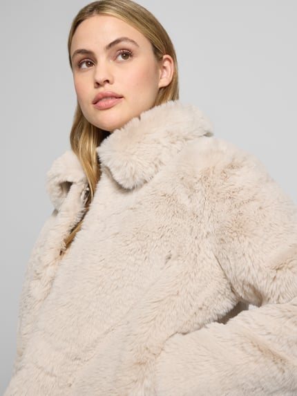 Vrouwenmodel draagt Jacke aus Kunstfell mit Eingrifftaschen van Milano Italy in beige, zachte textuur, regular fit, Nahaufnahme bovenlichaam.