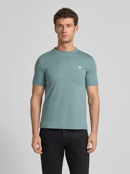 Männermodel trägt T-Shirt mit Label-Stitching und Rundhalsausschnitt von Emporio Armani in Hellblau, Slim Fit, Oberkörperansicht von vorne.