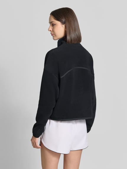 Frauenmodel trägt Relaxed Fit Pullover Troyer-Kragen Modell 'Polar' von Fabletics, schwarze Fleecejacke, überschnittene Schultern, Langarm, Kängurutasche, weiche Textur, Damen Fleecejacke, Ganzkörperansicht Rückansicht.