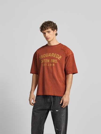 Männermodel trägt T-Shirt mit verstärktem Schultern von Dsquared2 in Rostbraun, Logo-Print, Rundhalsausschnitt, Oberkörperansicht von vorne.