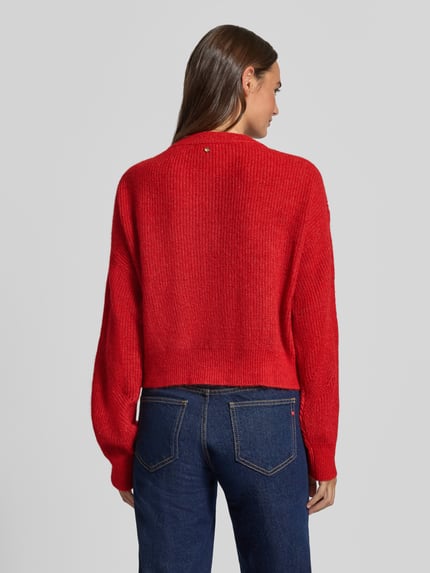 Frauenmodel trägt Regular Fit Strickjacke aus Alpaka-Woll-Mix Modell 'C_Fernad' von BOSS Orange in kräftigem Rot, grobe Strickstruktur, Ganzkörperansicht Rückansicht.