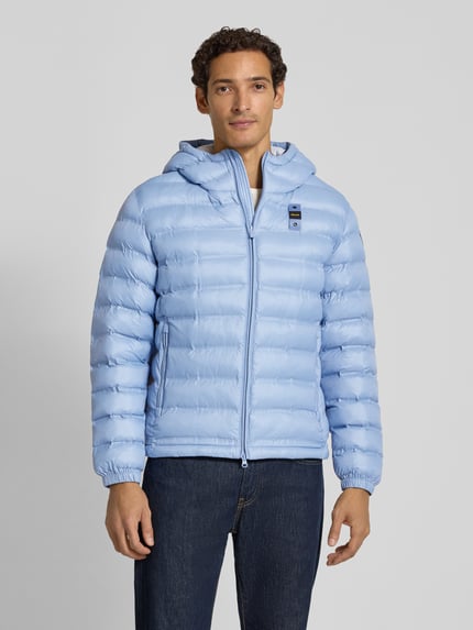 Männermodel trägt Steppjacke mit Zweiwege-Reißverschluss Modell 'CHARLES' von Blauer USA in Hellblau, Regular Fit, Ganzkörperansicht von vorne. Rückenlänge 67 cm, Schulterbreite 64 cm, Brustweite 53 cm, Ärmellänge 66 cm, Kapuze, Reißverschlusstaschen, Label-Detail, glatte texturierte Oberfläche.