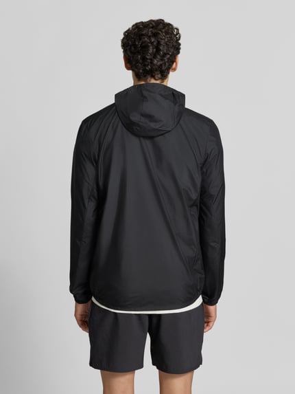 Männermodel trägt schwarze Regular Fit Trainingsjacke mit Logo-Print Modell 'Core' von ASICS TIGER, glatte Struktur, Ganzkörperansicht Rückansicht.