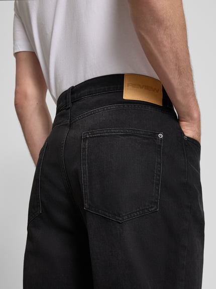 Mężczyznamodel prezentuje Baggy Jeans in schwarzer Waschung und klassischem 5-Pocket-Design von REVIEW, mieszanka bawełny i elastanu, krój baggy, czarny, 5 kieszeni, zapięcie na guzik i zamek błyskawiczny, szerokość w rozmiarze 32: 42 cm, długość wewnętrzna nogawki w rozmiarze 32: 76 cm, ujęcie z tyłu, detal.