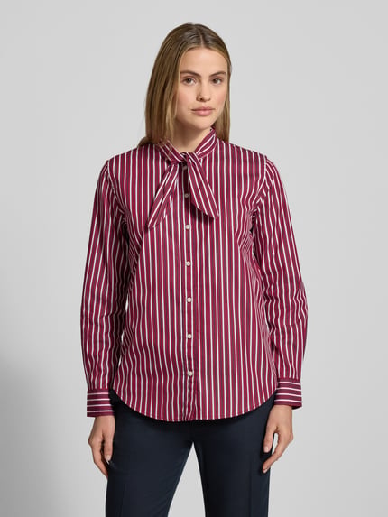 Frauenmodel trägt Hemdbluse mit Knopfleiste Modell 'NUSILA' von Lauren Ralph Lauren, Reine Baumwolle, Lockerer-Schnitt, Schleifen-Detail, gestreiftes Muster in Rot und Weiß, Ganzkörperansicht von vorne.