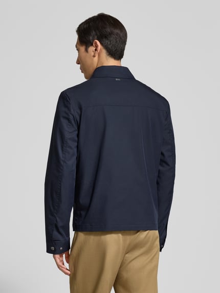 Mężczyznamodel nosi Jacke mit Pattentaschen und Zweiwege-Reißverschluss od bugatti, granatowy bawełniany materiał, prosty krój, patki, zamek dwukierunkowy, długość tyłu w rozmiarze 50: 67 cm, szerokość ramion w rozmiarze 50: 45 cm, szerokość klatki piersiowej w rozmiarze 50: 57 cm, długość rękawa w rozmiarze 50: 70 cm, zdjęcie całej sylwetki z tyłu