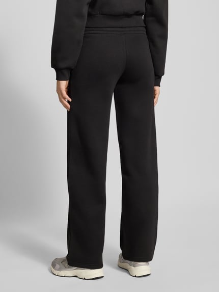 Vrouwenmodel draagt zwarte Sweatpants met elastische tailleband van Review, los model met labelprint en steekzakken, full body achteraanzicht.