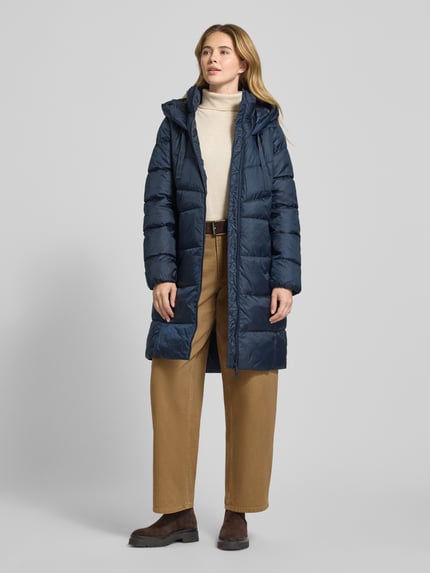 Frauenmodel trägt Regular Fit Steppmantel mit Kapuze von s.Oliver RED LABEL in Optik: Unifarben, mit Zweiwege-Reißverschluss, Label-Stitching, Langarm, elastischer Ärmelabschluss, Reißverschlusstaschen, Ganzkörperansicht von vorne.