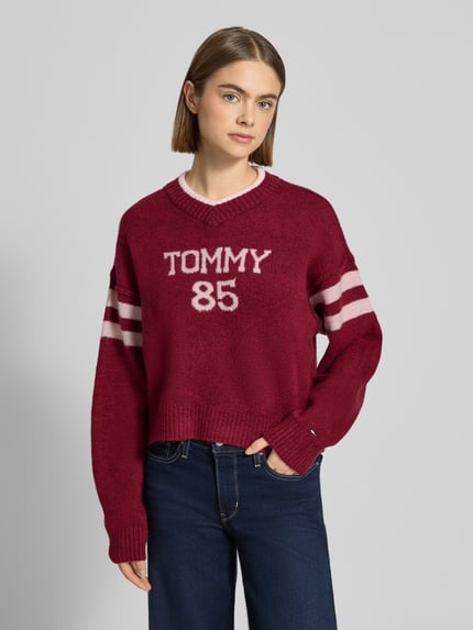 Vrouwenmodel draagt Oversized Strickpullover mit Woll-Anteil van Tommy Jeans, look: effen, oversized pasvorm, labelopschrift en intarsia, ronde hals en V-hals, lange mouwen, geribde boorden, knitweartextuur, ganzkörperansicht van voren.