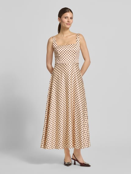 Frauenmodel trägt Cocktailkleid mit Karree-Ausschnitt und Bindegürtel von Jake*s Cocktail mit A-Linie, Midilänge, beige mit schwarzen Punkten, breite Träger, Rückansicht, Ganzkörperansicht von vorne.