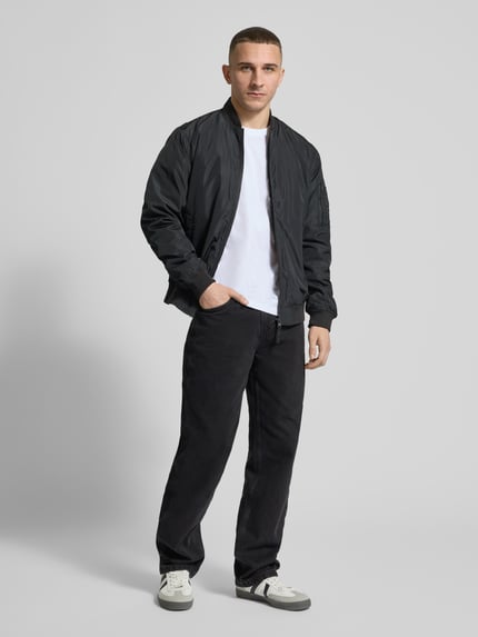 Männermodel trägt Baggy Jeans im 5-Pocket-Design mit Logo-Stitching von KARL KANI in Schwarz auf weißem Hintergrund, Ganzkörperansicht von vorne. Reine Baumwolle, Baggy Fit, Knopf- und Reißverschluss, entspannte Silhouette.