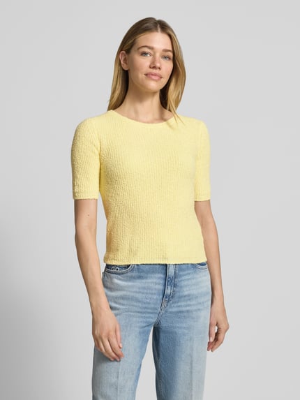 Modelka nosi T-Shirt in Strick-Optik mit Rundhalsausschnitt von Rich & Royal, damski t-shirt, mieszanka bawełny, krój straight fit, imitacja dzianiny, okrągły dekolt, długość tyłu w rozmiarze S: 50 cm, długość rękawów w rozmiarze S: 28 cm, jasny żółty kolor, teksturowana powierzchnia, widok całej sylwetki z przodu.