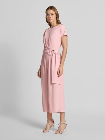 Modelka kobieca ma na sobie Jumpsuit mit Stretch-Anteil od Betty Barclay w kolorze jasnoróżowym, z paskiem w talii, krótkie rękawy, krój regular fit, długość 7/8, okrągły dekolt, gładka faktura, szerokość w rozmiarze 36: 37 cm, długość całkowita 127 cm, zdjęcie całej sylwetki z przodu.