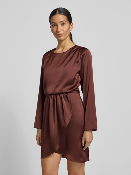 Frauenmodel trägt knielanges Cocktailkleid mit Rundhalsausschnitt von Rinascimento aus braunem Satin, körpernahe Passform, asymmetrischer Saum, Rückenlänge bei Größe S 91 cm, Brustweite 47 cm, Ärmellänge 59 cm, Ganzkörperansicht von vorne.