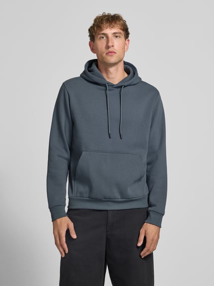 Männermodel trägt Hoodie mit Känguru-Tasche Modell 'BRADLEY' von JACK & JONES in Grau, lockerer Schnitt, Ganzkörperansicht von vorne.