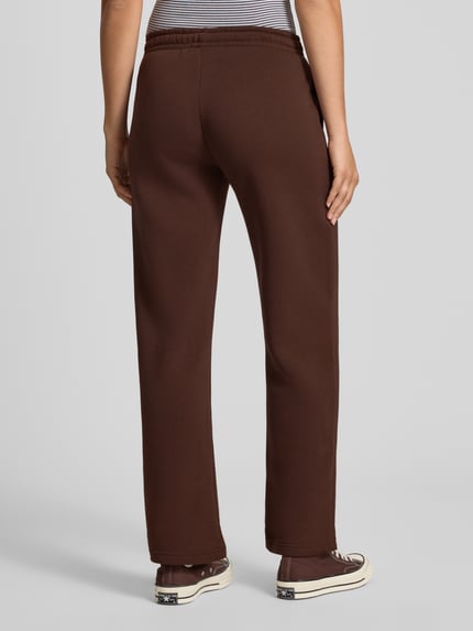 Frauenmodel trägt Wide Fit Sweatpants aus Baumwoll-Mix Modell 'Iconic' von Gina Tricot in Braun, elastischer Bund, Ganzkörperansicht Rückansicht.