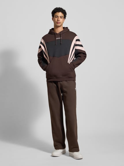 Męski model nosi Straight Fit Sweatpants mit Logo-Stitching od adidas Originals, bawełniane, elastyczny pas, widok całej sylwetki z przodu.