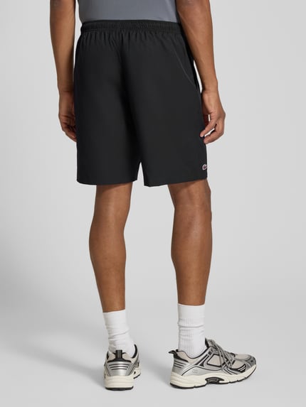 Männermodel trägt schwarze Relaxed Fit Shorts mit Logo-Patch von Lacoste, Herren Sportshorts, locker geschnitten, Ganzkörperansicht Rückansicht.
