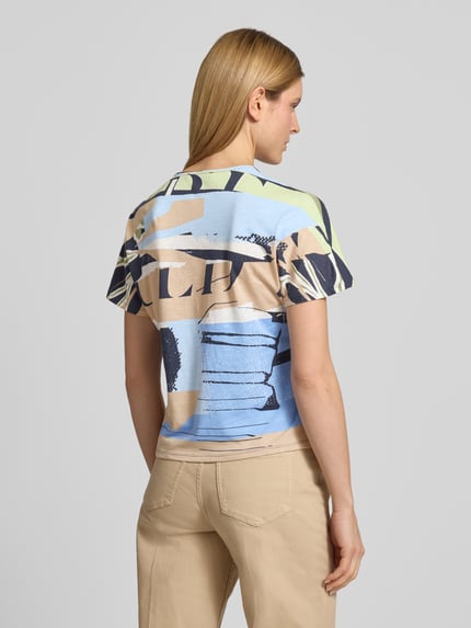 Modelka nosi T-Shirt im Allover-Look mit Rundhalsausschnitt von Betty Barclay, damski t-shirt z mieszanki bawełny i mikromodalu, krój regular fit, wzór na całej powierzchni, okrągły dekolt, długość tyłu w rozmiarze 36: 56 cm, jasnoniebieskie, beżowe i granatowe barwy, tekstura miękka, całkowity widok z tyłu.