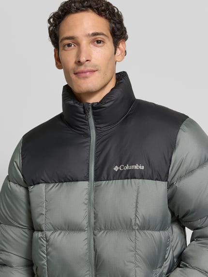 Männermodel trägt Regular Fit Jacke in Stepp-Optik Modell 'Puffect™' von Columbia, zweifarbig, Logo-Print, Nahaufnahme Oberkörper.
