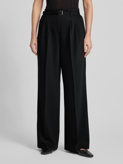 Frauenmodel trägt schwarze Stoffhose mit Gesäßtaschen von More & More, lockerer Schnitt, Stoffgürtel, Nahaufnahme Oberkörper, Material-Mix mit Viskose-Anteil, französische Eingrifftaschen.