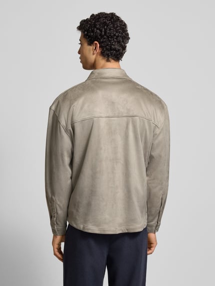 Męski model nosi Relaxed Fit Hemdjacke mit Brusttaschen und Label-Stitching od Pegador z weluru, kolor beżowy, krój relaxed fit, kołnierzyk typu kent, listwa guzikowa, kieszenie na piersi, wyhaftowane logo, długość tyłu 70 cm przy rozmiarze M, widok całej sylwetki od tyłu.