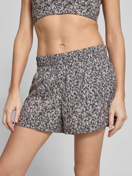 Frauenmodel trägt Running Shorts mit elastischem Bund Modell 'kallin' von VARLEY, graues Muster, Material-Mix mit Stretch-Anteil, Relaxed-Fit, Nahaufnahme Oberkörper. Bundweite bei Größe S: 40 cm, Innenbeinlänge: 8 cm.