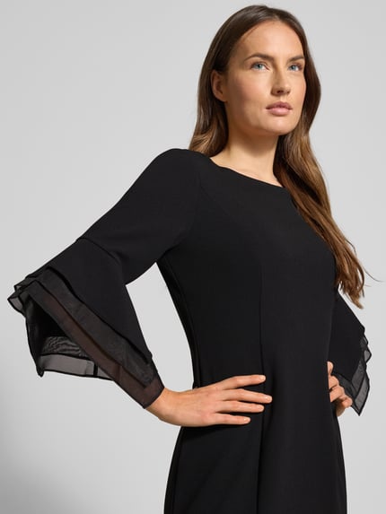 Kobieta modelka nosi Knielanges Cocktailkleid mit Trompetenärmeln od Adrianna Papell, mieszanka materiałów z dodatkiem streczu, prosty krój, długość do kolan, rozszerzane rękawy, okrągły dekolt, czarny kolor, miękka tekstura, zbliżenie na górną część ciała.