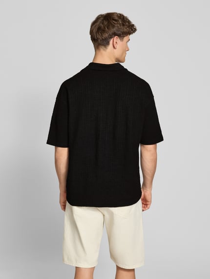 Männermodel trägt Regular Fit Freizeithemd mit Label-Patch Modell 'LIBCO' von Pegador, Schwarz, Material-Mix, Rückenansicht, Ganzkörperansicht Rückansicht. Rückenlänge bei Größe M: 72 cm, Schulterbreite: 41 cm, Ärmellänge: 35 cm, Kurzärmelig, Reverskragen, Knopfleiste.