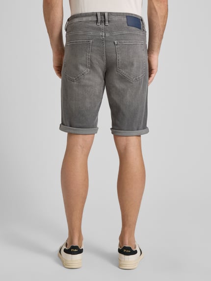 Męski model nosi Regular Fit Jeans Bermudas aus Baumwoll-Mix von Tom Tailor w kolorze szarego denimu, krój regular fit, z naszywką z logo, 5 kieszeni, mieszanka bawełny, widok całej sylwetki od tyłu.