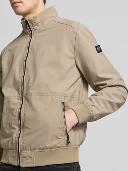 Männermodel trägt Regular Fit Jacke mit Stehkragen von Lerros in Beige, elastischer Material-Mix, Logo-Detail, Nahaufnahme Oberkörper.