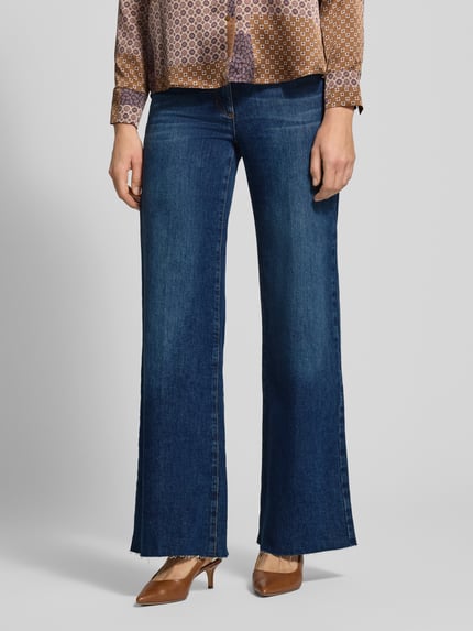 Frauenmodel trägt Flared Fit Jeans aus elastischem Baumwoll-Mix mit Gürtelschlaufen von Luisa Cerano, blaue Farbe, sichtbare Eingrifftaschen und Gesäßtaschen, glatte Textur, Produktdetails wie Knopf- und Reißverschluss, Bundweite 39 cm, Innenbeinlänge 83 cm, Nahaufnahme Oberkörper bis Füße, Vorderansicht.