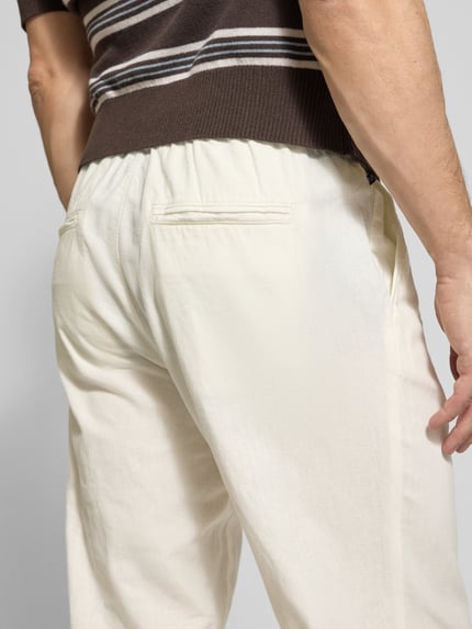 Männermodel trägt Straight Fit Leinenhose mit elastischem Bund Modell 'Barton' von Matinique, mieszanka lnu i bawełny, krój straight fit, elastyczny pas z tunelem, kieszenie z tyłu, szerokość w rozmiarze M 34 cm, długość wewnętrzna nogawki 78 cm, jasny kolor, gładka tekstura, zdjęcie z tyłu, detal pasa i kieszeni, zbliżenie