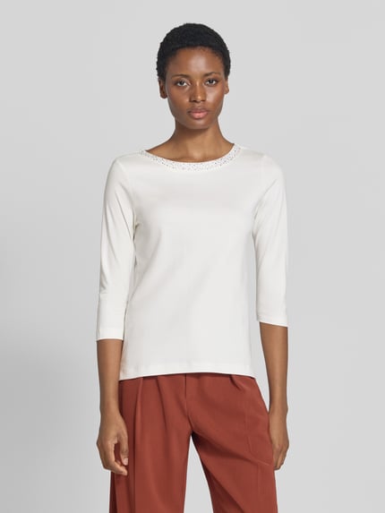 Frauenmodel trägt Regular Fit Shirt aus reiner Baumwolle von Christian Berg Woman mit Ziersteinen, U-Boot-Ausschnitt, 3/4-Arm, Weiß und glatte Textur, Ganzkörperansicht von vorne.
