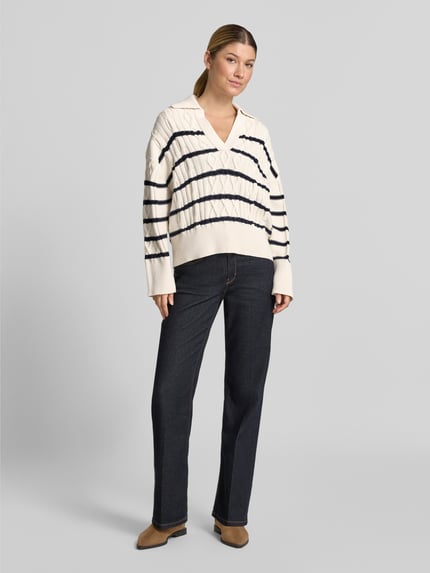 Modelka kobieca nosi kremowy Relaxed Fit Pullover aus Baumwoll-Mix Modell 'C_Farboria' od BOSS Orange z czarnymi paskami, ciemne jeansy, neutralne buty, jasne tło, widok całej sylwetki z przodu.