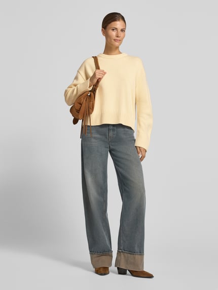 Frauenmodel trägt Strickpullover aus Woll-Mix Modell 'GRISUC' von MANGO in Creme, kombiniert mit weiter Jeans und braunen Schuhen, Ganzkörperansicht von vorne. Relaxed Fit, Rundhalsausschnitt, Rückenlänge 54 cm, Ärmellänge 62 cm.