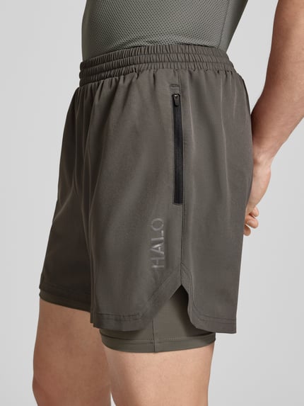 Mannenmodel draagt Shorts im 2-in-1-Look van HALO in grijs materiaalmix met stretch, regular fit, elastische band, detailopname zijkant.