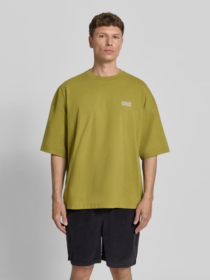 Männermodel trägt Herren T-Shirt mit Logo-Print Modell 'GIXY' von American Vintage in grün, Reine Baumwolle, Loose-Fit, Ganzkörperansicht von vorne.