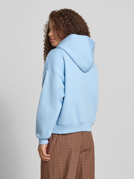 Frauenmodel trägt Hoodie mit Logo-Print und Känguru-Tasche von REVIEW, hellblauer Baumwoll-Mix, Loose-Fit, Kapuze, Ganzkörperansicht Rückansicht.