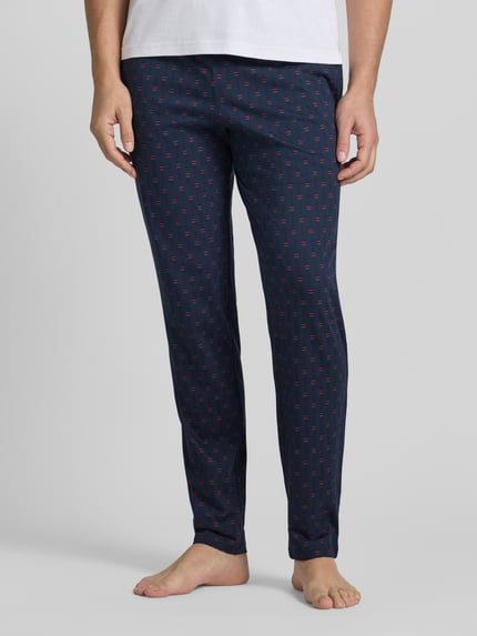 Männermodel trägt Sweatpants mit elastischem Bund von Schiesser aus reiner Baumwolle, lockerer Schnitt, Dunkelblau mit Muster, Nahaufnahme Unterkörper.