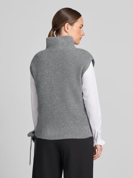 Frauenmodel trägt Relaxed Fit Pullunder aus reinem Kaschmir mit Stehkragen von Christian Berg Woman in Grau, Zierschleife am Saum, Ganzkörperansicht Rückansicht.