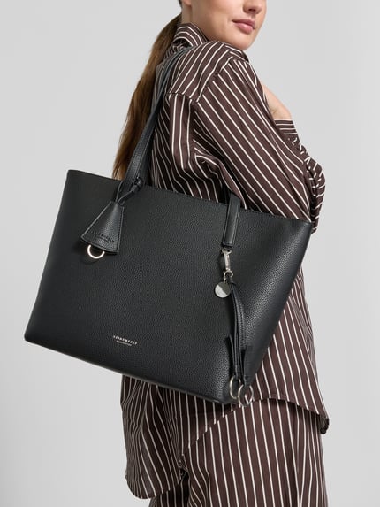 Frauenmodel trägt Shopper mit Label-Detail Modell 'LOHJA' von Seidenfelt in Schwarz, grobe Struktur, Anhänger, Ganzkörperansicht von vorne. Hauptfach mit Reißverschluss, Lange Tragegriffe, Reißverschlussfach innen, Breite 41 cm, Länge 29 cm, Tiefe 68 cm, Länge Schulterriemen 12 cm.