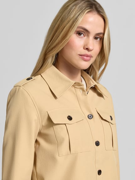 Frauenmodel trägt Longline Langarmbluse mit Schulterklappen von BAUM & PFERDGARTEN, unifarbene Webware mit Struktur, Zierknöpfe, Brusttaschen, Nahaufnahme Oberkörper.