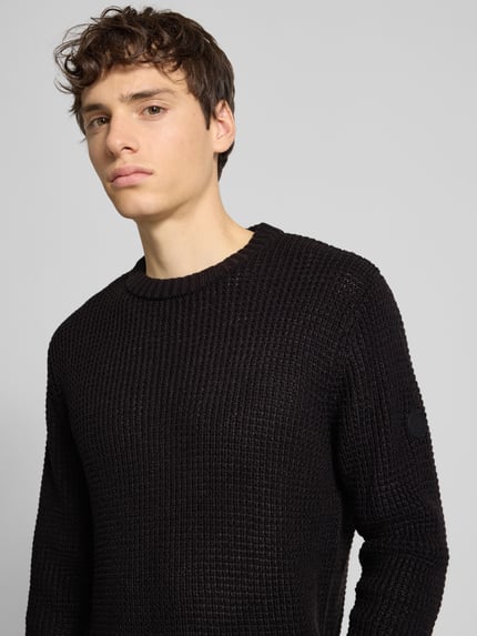 Männermodel trägt schwarzen Strickpullover mit gerippten Abschlüssen Modell 'LIAM' von Jack & Jones, Baumwoll-Mix, Nahaufnahme Oberkörper.
