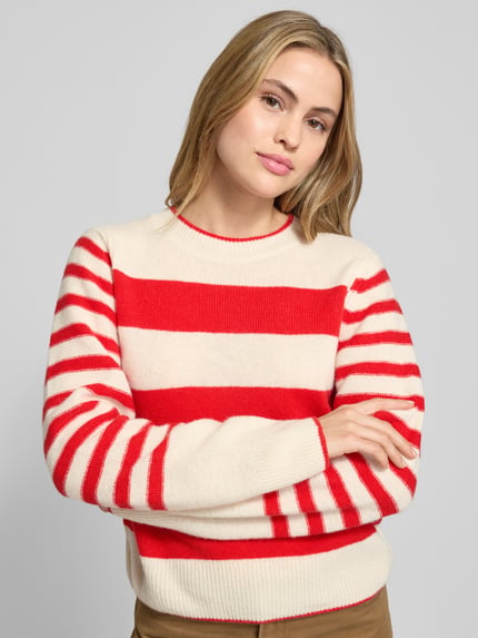 Vrouwenmodel draagt Regular Fit Strickpullover aus reiner Schurwolle van Marc O'Polo, rood-wit gestreept, lange mouwen, gebreide textuur. Nahaufnahme bovenlichaam.